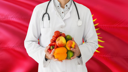 Doctor is holding fruits and vegetables in hands with Kyrgyzstan flag background. National healthcare concept, medical theme.
