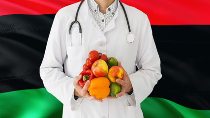 Doctor is holding fruits and vegetables in hands with Libya flag background. National healthcare concept, medical theme.