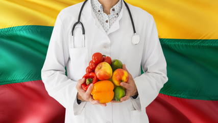 Doctor is holding fruits and vegetables in hands with Lithuania flag background. National healthcare concept, medical theme.