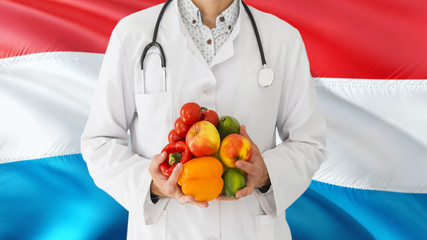 Doctor is holding fruits and vegetables in hands with Luxembourg flag background. National healthcare concept, medical theme.