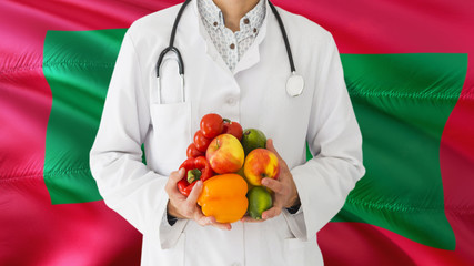 Doctor is holding fruits and vegetables in hands with Maldives flag background. National healthcare concept, medical theme.