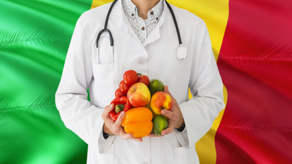 Doctor is holding fruits and vegetables in hands with Mali flag background. National healthcare concept, medical theme.