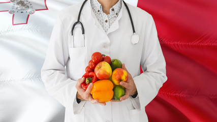 Doctor is holding fruits and vegetables in hands with Malta flag background. National healthcare concept, medical theme.