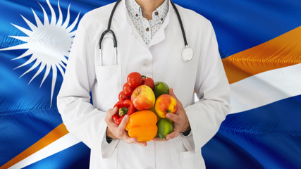 Doctor is holding fruits and vegetables in hands with Marshall Islands flag background. National healthcare concept, medical theme.