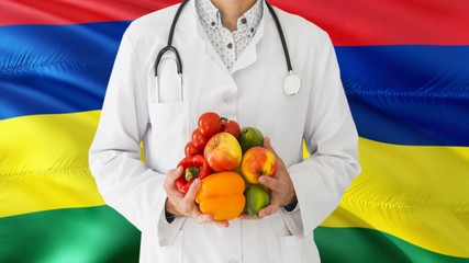 Doctor is holding fruits and vegetables in hands with Mauritius flag background. National healthcare concept, medical theme.