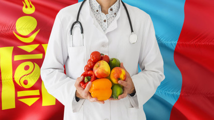 Doctor is holding fruits and vegetables in hands with Mongolia flag background. National healthcare concept, medical theme.