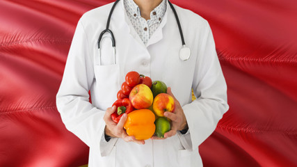 Doctor is holding fruits and vegetables in hands with Montenegro flag background. National healthcare concept, medical theme.