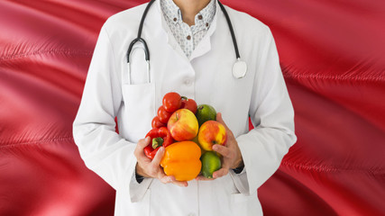 Doctor is holding fruits and vegetables in hands with Morocco flag background. National healthcare concept, medical theme.