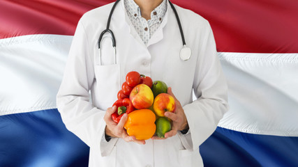 Doctor is holding fruits and vegetables in hands with Netherlands flag background. National healthcare concept, medical theme.