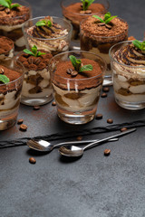 Group of portions of Classic tiramisu dessert in a glass cup on stone board on concrete background