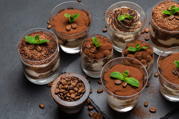 Group of portions of Classic tiramisu dessert in a glass cup on stone board on concrete background