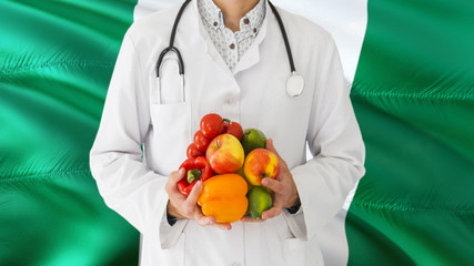 Doctor is holding fruits and vegetables in hands with Nigeria flag background. National healthcare concept, medical theme.