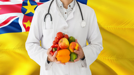 Doctor is holding fruits and vegetables in hands with Niue flag background. National healthcare concept, medical theme.