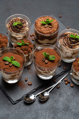 Group of portions of Classic tiramisu dessert in a glass cup on stone board on concrete background