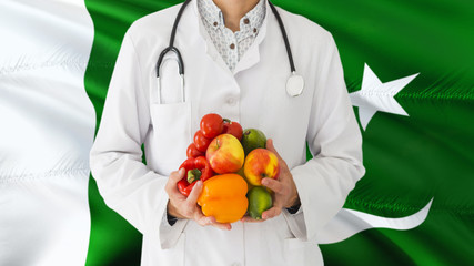 Doctor is holding fruits and vegetables in hands with Pakistan flag background. National healthcare concept, medical theme.