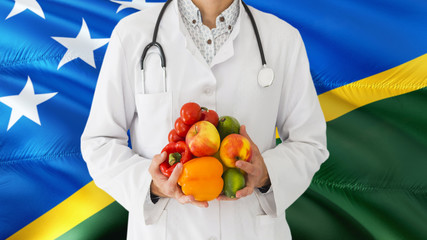 Doctor is holding fruits and vegetables in hands with Solomon Islands flag background. National...