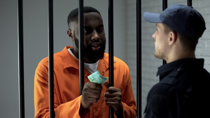 African american prisoner giving euro cash to guard, corruption in jail, bribe