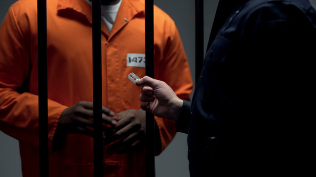 Corrupt officer giving black imprisoned criminal blade, revolt preparation