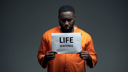 Afro-american imprisoned male holding life sentence sign, looking to camera