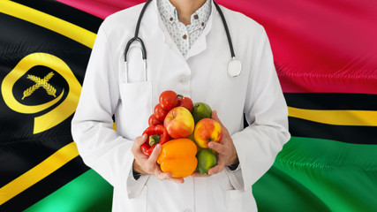 Doctor is holding fruits and vegetables in hands with Vanuatu flag background. National healthcare...