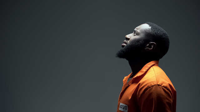 Afro-american imprisoned male praying looking up at light, talking to god, faith