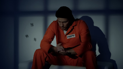 Unhappy Caucasian male prisoner feeling guilty about crime, thinking in cell