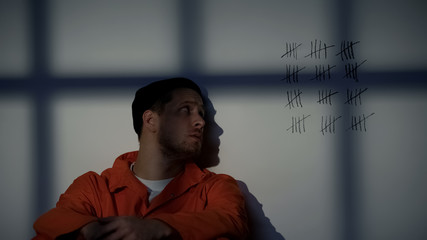 Male prisoner looking at crossed lines on cell wall, serving long imprisonment