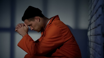 Caucasian imprisoned male praying in cell, feeling guilty and asking for mercy