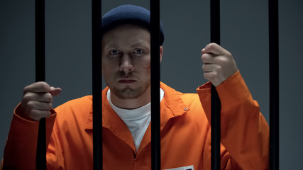 Dangerous imprisoned criminal with scar on face holding bars looking at camera