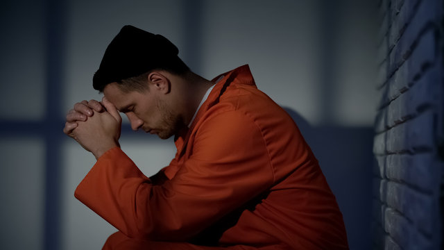 Caucasian imprisoned male praying in cell, feeling guilty and asking for mercy