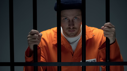Disappointed male prisoner holding cell bars, losing hope for amnesty, justice