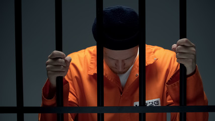 Prisoner holding bars and leaning head, feeling depressed, psychological rehab