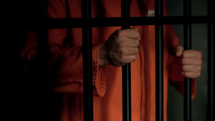 Aggressive male prisoner holding bars with injured hands, violence in jail