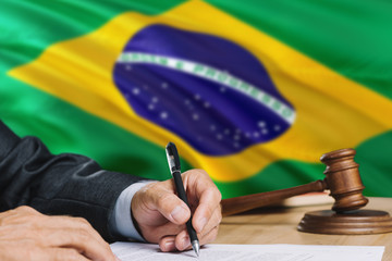 Judge writing on paper in courtroom with Brazil flag background. Wooden gavel of equality theme and...