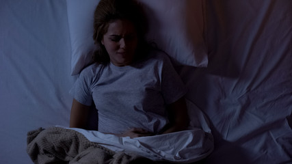 Young woman waking up at night because of spasm in stomach, gastritis, top-view