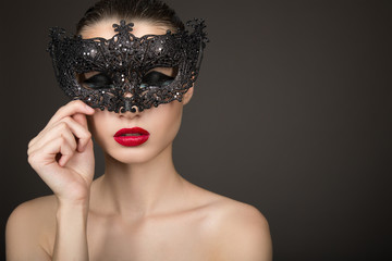 Fashion woman with long hair and red lipstick with a black mask. Dark background. Carnival, holiday