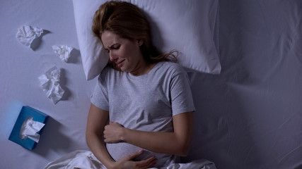 Lonely pregnant woman crying in bed, holding belly, relationship problems