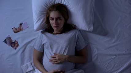 Sad expecting lady lying in bed with torn photo of ex-husband, loneliness