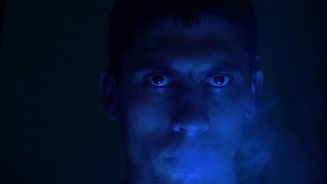 Young handsome man with stubble letting go smoke from lungs while being on the neon lighting wall background. man lets out smoke. Smoking. Close-up. 
