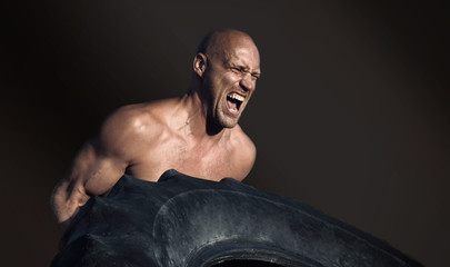 Shirtless man flipping heavy tire outside gym. Workout.
