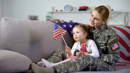 American female veteran and little daughter with flag watching military march