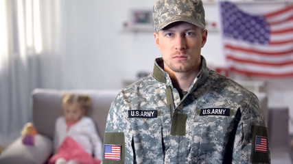 Serious military man looking at camera, little daughter on background, support