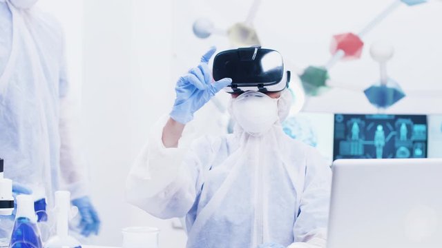 Female scientis with coverall equipment and virtual reality headset touching in the air in modern science laboratory. Sophisticated modern technology in science laboratory.