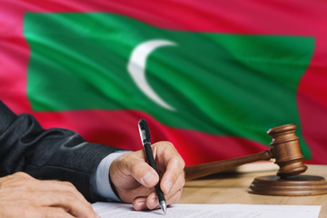 Judge writing on paper in courtroom with Maldives flag background. Wooden gavel of equality theme and legal concept.