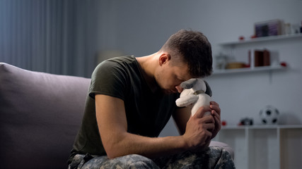 Melancholic male soldier holding toy dog, missing child after divorce, lonely