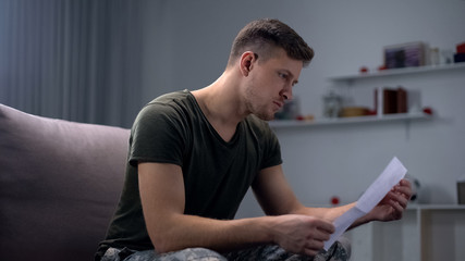 Male soldier reading letter from family, armed forces duty, feeling support