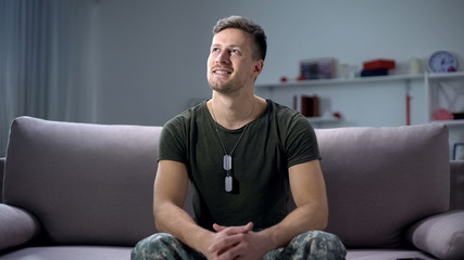 Inspired soldier sitting on sofa and dreaming about long-awaited holiday, smile