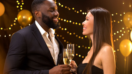 Cheerful romantic couple clinking glasses of champagne at birthday party, flirt