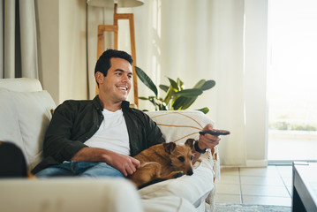 Relaxed man lying with his dog on sofa watching tv in living roo
