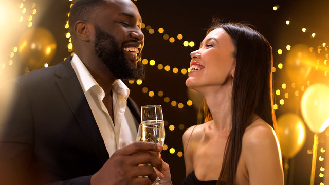 Romantic young couple clinking champagne and smiling each other, having fun - Powered by Adobe